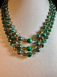 Attractive vintage lucite and glass Japanese 3 strand bib necklace. Large green lucite bead from 13mm down to 7mm round with similar size twisted beads. The addition of 8mm transparent green faceted glass beads and glass seed bead spacers really clinches the elegant look. The complete shortest length with 3 inch adjustable extension is 19 inches. Stamped Japan on the silver tone clasp. Good condition with little wear and a hook clasp. (B484) Green Multi-strand Costume Jewelry, Vintage Green Double Strand Necklaces, Vintage Multi-strand Green Beaded Necklaces, Vintage Green Double Strand Necklace, Vintage Green Multi-strand Beaded Necklaces, Vintage Green Multi-strand Beaded Necklace, Green Large Beads Round Jewelry, Green Round Beads Costume Jewelry, Vintage Green Jewelry With Faceted Beads