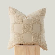 a white pillow on top of a wooden block with a black and beige patchwork pattern