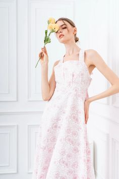 a woman in a pink and white dress holding a yellow flower up to her face