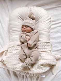 a baby is sleeping in a beanie and sweater on a white blanket with pillows