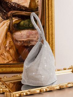 a silver mesh bag sitting on top of a table next to a framed art piece