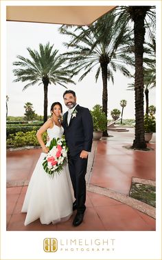 a bride and groom pose for a photo in front of palm trees