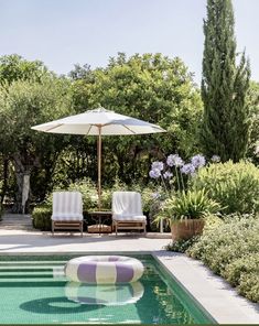 two lawn chairs sitting next to a swimming pool with an umbrella in the middle of it