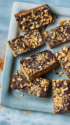 several pieces of brownie on a blue plate next to some nuts and chocolate chips