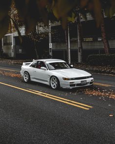 a white car is parked on the side of the road in front of some trees