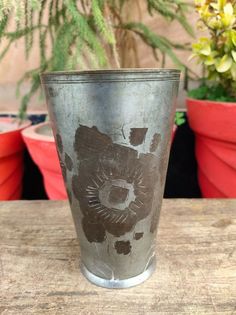 a metal vase sitting on top of a wooden table next to potted planters