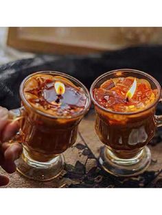 two mugs filled with hot chocolate and topped with a lit candle, on top of a table