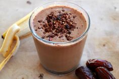 a smoothie in a glass next to two bananas and dates on a wooden table