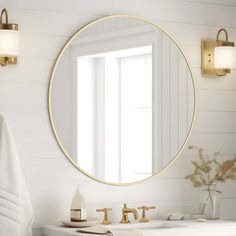 a bathroom with white walls, gold fixtures and a round mirror on the wall above the sink