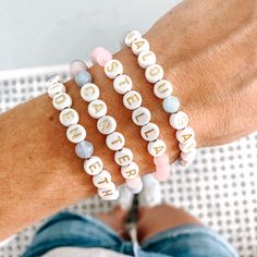 three bracelets with letters on them sitting on a person's arm, one is white and the other has pink beads