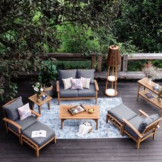 an outdoor living room with blue cushions and wooden furniture on a deck surrounded by greenery