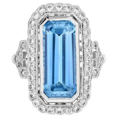 Drawing inspiration from the pattern of the bygone ear, this Art Deco-inspired blue topaz ring is crafted in 18k white gold. Glimmering round diamonds create a brilliant halo around the emerald-cut blue topaz. Additional diamond accents embellish the shoulder for extra shimmer. Ring Information Style: Art-deco Metal: 18K White Gold Weight: 5.18 g. (approx. total weight) Center Gemstones Type: Blue Topaz Shape: Emerald Cut Size: 1696 mm. Number: 1 Weight: 7 Carat (approx. total weight) Accent Gemstones Type: Diamond Shape: Round Average Color: H Average Clarity: SI Size: 1.3 – 1.6 mm. Number: 42 Weight: 0.66 Carat (approx. total weight) This ring will be made to your order in 1-2 weeks, contact us to find out more. An attractive ring box is included.  Most of our rings can be sized to any f Formal Light Blue Diamond Ring, Luxury Diamond White Topaz Ring With Gemstone, Luxury Platinum Topaz Ring With Accent Stones, Luxury Platinum Topaz Gemstone Ring, Luxury Blue Topaz Ring With Diamond Accents, Luxury White Gold Topaz Ring With Halo Setting, Exquisite Diamond Topaz Ring With Accent Stones, Luxury Blue Topaz Halo Ring, Luxury Light Blue Topaz Ring With Center Stone