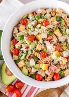 a white bowl filled with pasta salad next to sliced avocado and cherry tomatoes