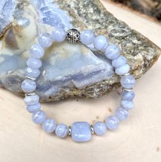 "Here is a beautiful calming BLUE LACE AGATE STRETCH BRACELET with silver plated accent beads. Created with high quality natural stone beads, the 12mm sized square center bead is surrounded by 8mm round and faceted rondelle beads. Blue lace agate is a wonderful tool to get stress out of your life, is an excellent crystal for public speakers, and is associated with the throat chakra. The bracelet is shown in size 7\", but is available in sizes 6\"- 8\". All jewelry arrives to you in an attractive Silver Agate Stretch Bracelet, Silver Agate Crystal Bracelet With Round Beads, Silver Beaded Bracelets With 8mm Beads For Meditation, Spiritual Light Blue Beaded Bracelets, Silver Agate Stretch Bracelet With Natural Stones, Light Blue Gemstone Beaded Bracelets For Healing, Silver Stretch Bracelet With Natural Stones For Healing, Silver Beaded Bracelets With Gemstone Beads For Meditation, Silver Gemstone Beaded Bracelets For Meditation