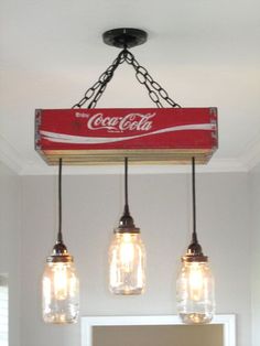 three mason jar lights hanging from a light fixture in a bathroom with coca - cola sign