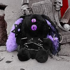 a black and purple teddy bear with chains around it's neck sitting in front of a grave