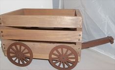 a wooden toy wagon with wheels on the floor next to a white sheeted wall