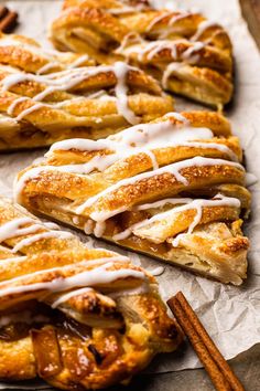 cinnamon rolls with icing on top and cinnamon sticks next to them sitting on wax paper