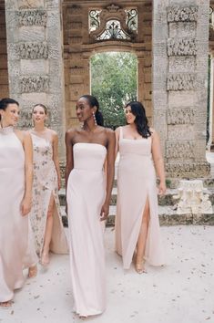 four bridesmaids standing in front of an old building with stone pillars and doors