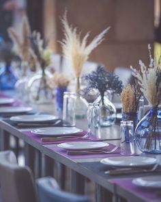 a long table is set with plates and vases filled with dried flowers, silverware and candlesticks