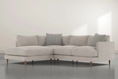 a white couch with pillows on it in front of a white wall and grey floor