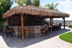 an outdoor bar with stools and a thatched roof on a brick patio area