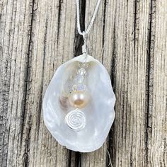 This beautiful pendant is made from a natural white oyster found on the beaches in the Cape May area. A spectacular metallic fresh water pearl is nestled inside the oyster shell showing off the treasure inside. The shell was then wire wrapped with sterling silver wire. The pendant measures 2 inches in length from the top of the bail and 1 inches wide. The pendant is on a 16" sterling silver box chain but other lengths are available in the below options. Elegant Silver Abalone Shell, Silver Shell With Pearl Pendant, Silver Shell Jewelry With Pearl Charm, Silver Abalone Shell Pendant Necklace, Silver Shell Necklace With Pearl Pendant, Silver Shell Necklace With Pearl Pendant As Gift, Silver Shell Necklace For Gift, Silver Shell Gift, Silver Wire Wrapped Pearl Necklace Gift