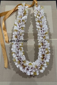 a white and gold flower lei with a ribbon around it's neck on a beige background