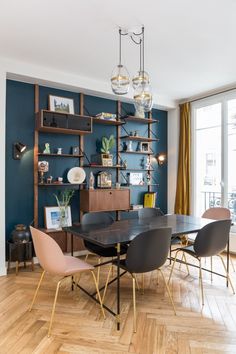 a dining room with blue walls and wooden flooring is furnished with modern chairs, shelving units and shelves