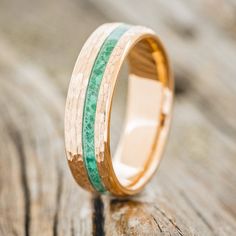 a wooden ring with green and gold inlays sitting on a piece of wood