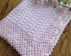 a pink crocheted blanket sitting on top of a wooden table next to flowers