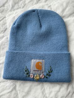 a blue beanie with an embroidered patch on the front and side, sitting on top of a bed