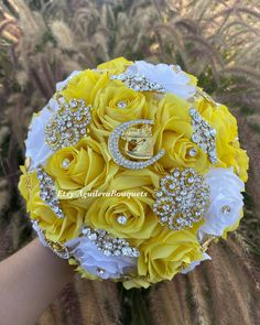 a bridal bouquet made with yellow roses and diaper covered brooches is held by someone's hand