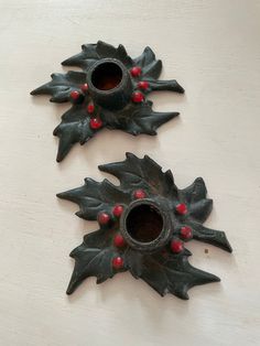 two metal objects with red berries on them sitting on a white table top, one is shaped like a leaf and the other is shaped like an acorny plant