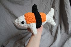 a hand holding a small crocheted fish with black, white and orange stripes