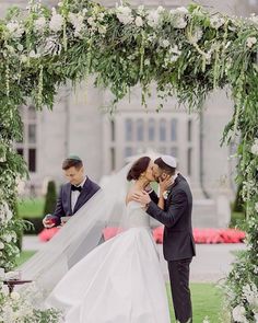 a bride and groom standing under an arch with greenery on the lawn at their wedding