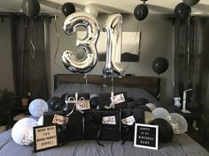 a bed topped with lots of black and white balloons next to a number three balloon