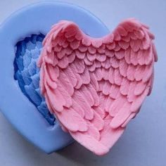 two pink and blue heart shaped molds on a white surface, one with an angel's wings