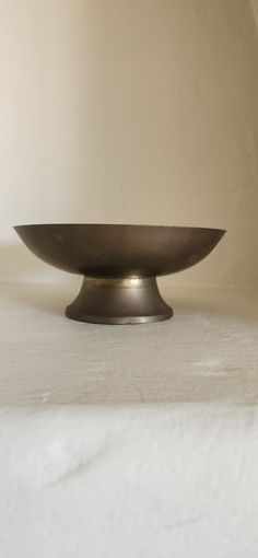 a metal bowl sitting on top of a white tablecloth covered counter next to a wall