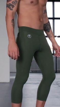 a shirtless man with tattoos standing in front of a window wearing green leggings