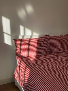 a bed with red and white striped sheets in a room next to a wooden floor