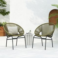 two chairs sitting next to each other in front of a white table and potted plant