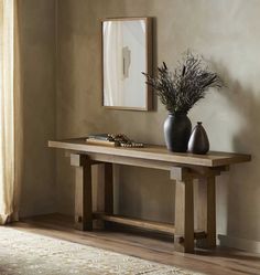 a wooden table with two vases on top of it next to a mirror and rug