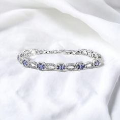 Indulge in the allure of timeless glamour with our Handmade Oval Tanzanite Stone Bracelet, a masterpiece of elegance meticulously crafted in 925 sterling silver. Embellished with tanzanite oval measuring 5 mm long by 3 mm wide in dimensions. Our artisans, with their unwavering commitment to excellence, have meticulously designed this bracelet to be a true work of art. The 925 sterling silver setting, enhanced by gold rhodium plating and moissanites, reflects a perfect blend of classic and contemporary design. Tanzanite, with its captivating violet-blue shades, is renowned for its unique and mesmerizing color. Tanzanite is believed to have spiritual properties, promoting calmness and enhancing communication. Tanzanite is exclusively found in Tanzania, making it a rare and precious gem. The Silver Tanzanite Bracelet Fine Jewelry, Silver Tanzanite Bracelet In Fine Jewelry Style, Elegant Silver Tanzanite Bracelets, Fine Jewelry Tanzanite Bracelets For Gift, Silver Tanzanite Bracelets For Formal Occasions, Sapphire Bracelets As A Gift, Moissanite Bracelet, Tanzanite Bracelet, Bracelet For Her