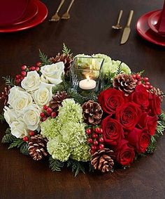 a christmas centerpiece on a table with red and white flowers, greenery, pine cones and candles