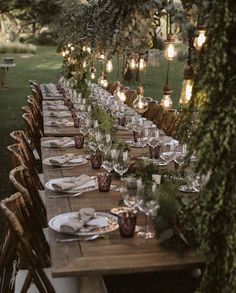 a long table is set up for an outdoor dinner party with candles and greenery