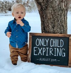 a little boy standing next to a tree in the snow