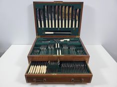 an open wooden box filled with silverware on top of a white tablecloth covered floor