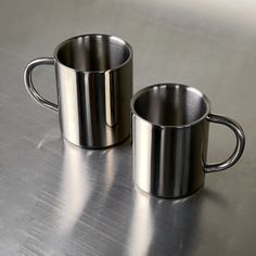 two stainless steel mugs sitting on top of a table