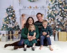 a family poses for a photo in front of christmas trees